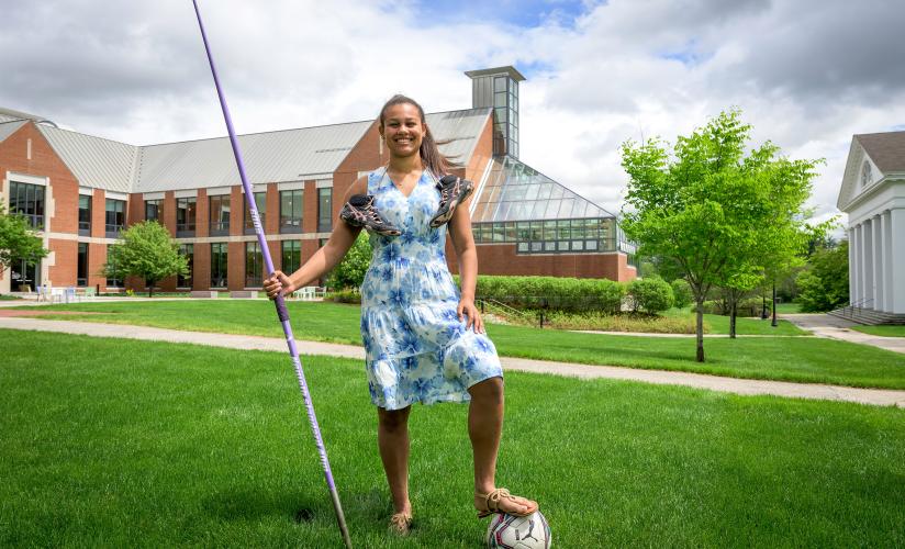 Cami Capdevila posing with javelin, soccer ball and cleats in front of Lindsay Center