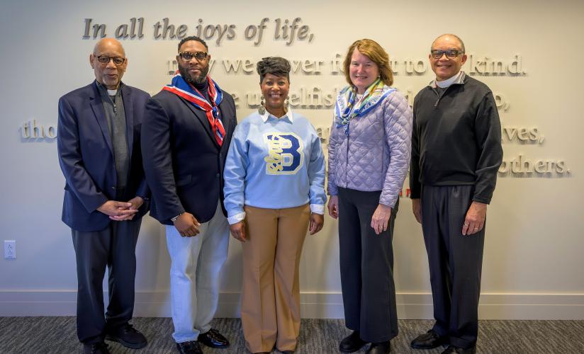 Rector Giles and Rev. Chuck Wynder pose with three visitors from the Bishop Walker School for Boys, standing in front of the School Prayer mounted on a wall in the Fleischner Family Admissions Center.