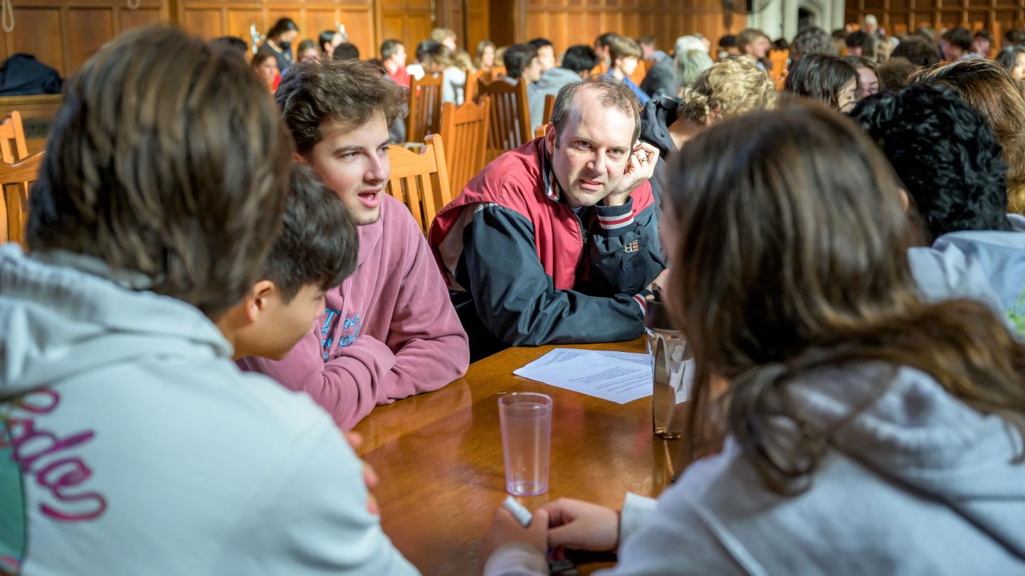 Teacher and students in discussion in dining hall.