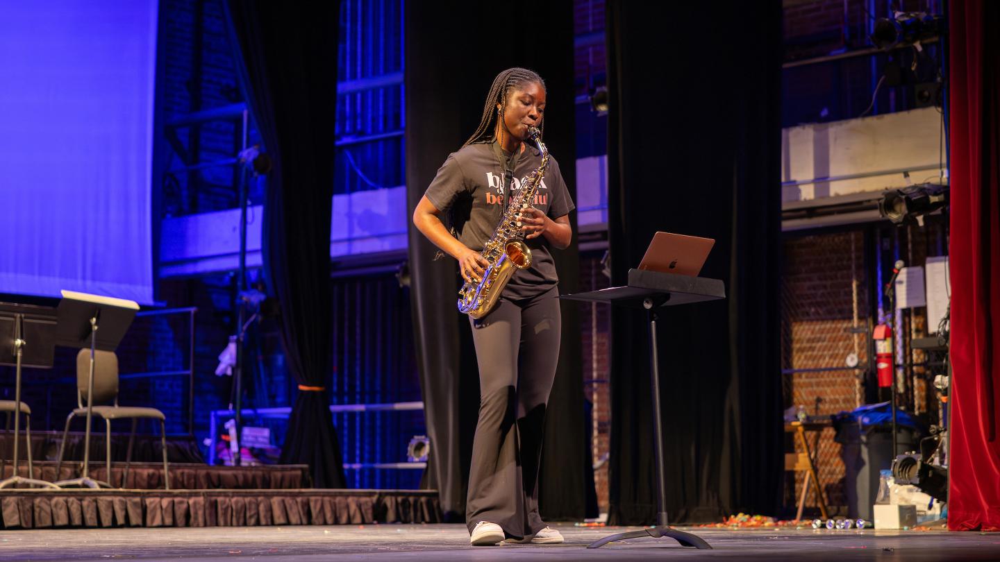 A student plays the saxophone on stage in Memorial Hall.